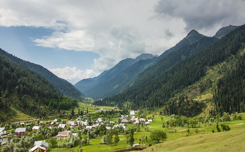 Wide view of Aru Valley village surrounded by mountains, forests, and green fields